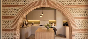 Cuisine vue à travers une arche en brique toulousaine, îlot au premier plan, réalisation MT Cuisine à Plaisance-du-Touch