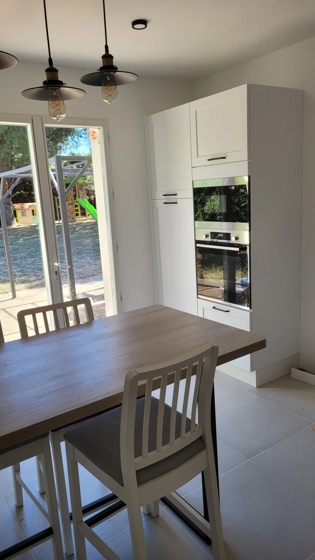 Coin repas sous suspensions devant une porte-fenêtre, réalisation MT Cuisine à Montgiscard