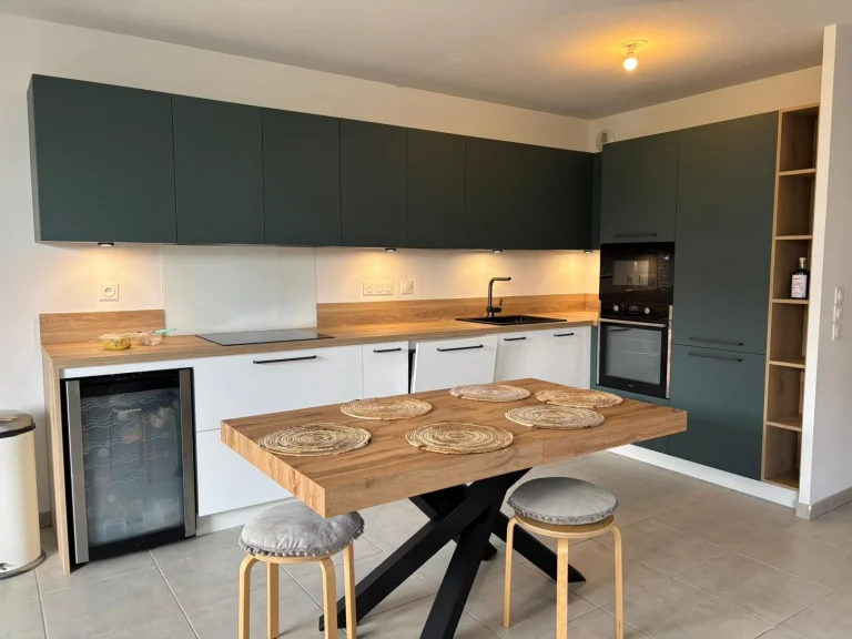 Cuisine à façades vert sauge avec table en bois et colonne de rangement, réalisation MT Cuisine à Toulouse