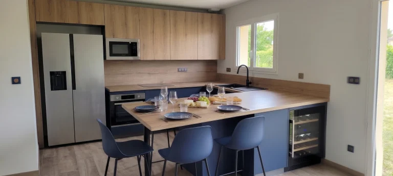 Îlot à façades bleues prolongé d'une table en bois, réfrigérateur américain et cave à vin, réalisation MT Cuisine à Saubens