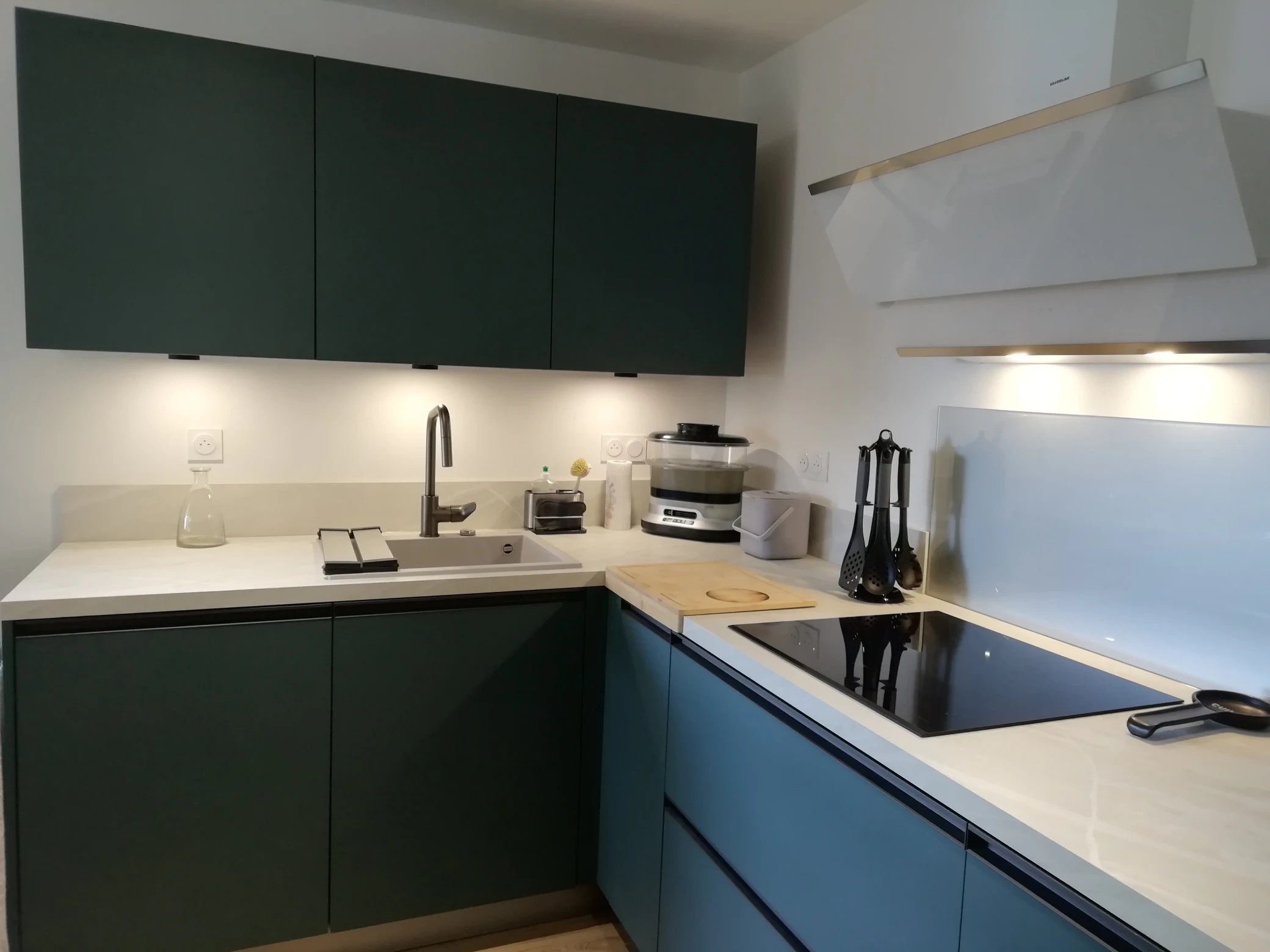 Cuisine en L à façades vert foncé avec plan de travail blanc et hotte, réalisation MT Cuisine à Toulouse