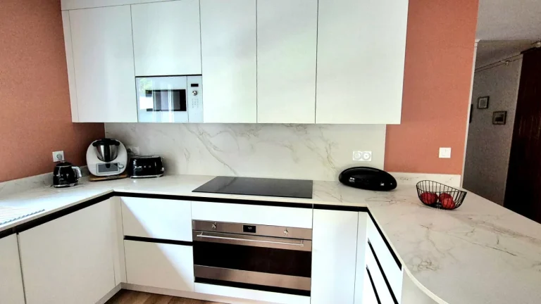 Cuisine blanche en L devant un mur terracotta, four et micro-ondes encastrés, réalisation MT Cuisine à Pompertuzat