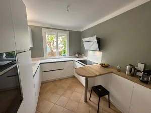 Cuisine blanche en U devant un mur vert, plan de travail clair et tablette en stratifié effet bois, réalisation MT Cuisine à Toulouse