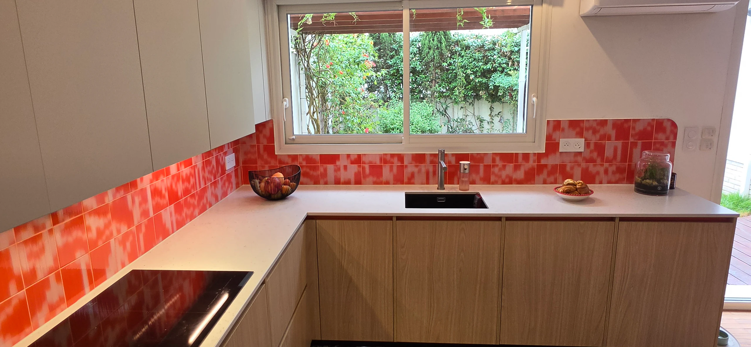 Plan de travail Silestone clair avec évier sous la fenêtre et faïence orange, réalisation MT Cuisine à Toulouse
