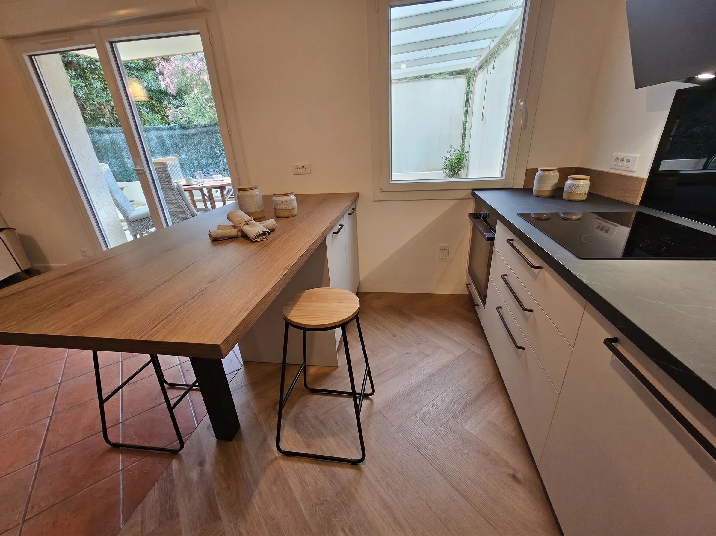 Cuisine blanche avec longue table en bois devant une verrière, réalisation MT Cuisine à Toulouse