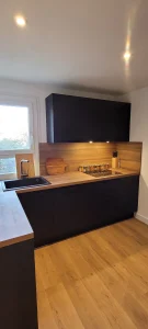 Cuisine à façades noires mates et plan de travail effet bois, vue depuis l’entrée, réalisation MT Cuisine à Pins-Justaret