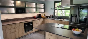 Cuisine d’aspect bois et gris avec meubles hauts vitrés éclairés et hotte îlot, réalisation MT Cuisine à Vigoulet-Auzil