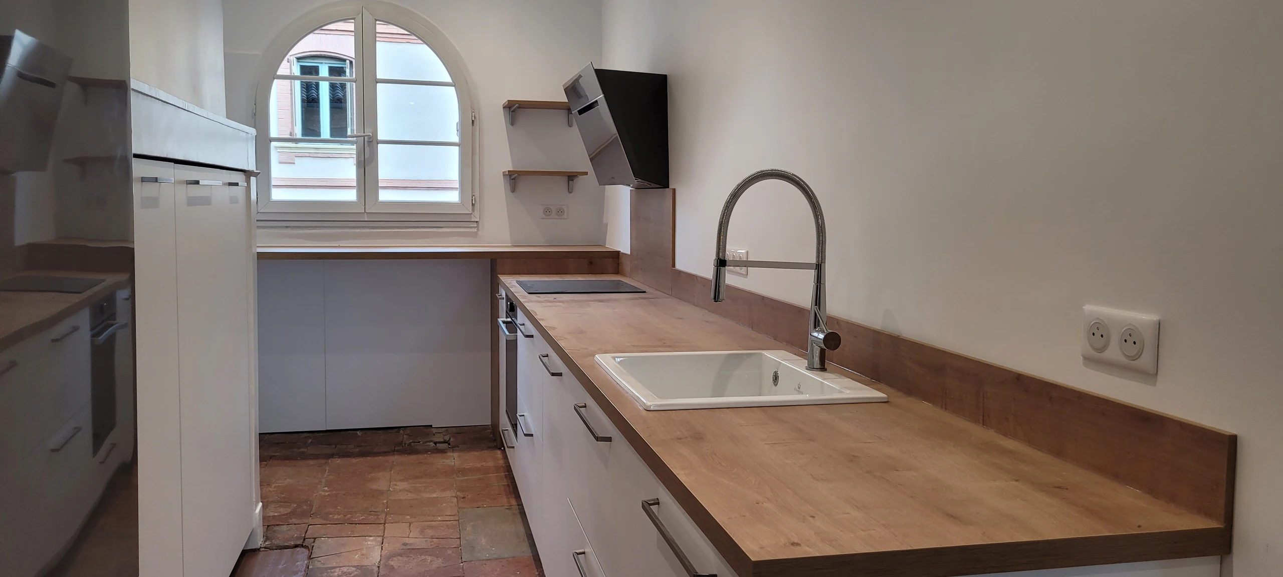 Cuisine linéaire blanche avec plan de travail effet bois, évier et fenêtre cintrée, réalisation MT Cuisine à Toulouse