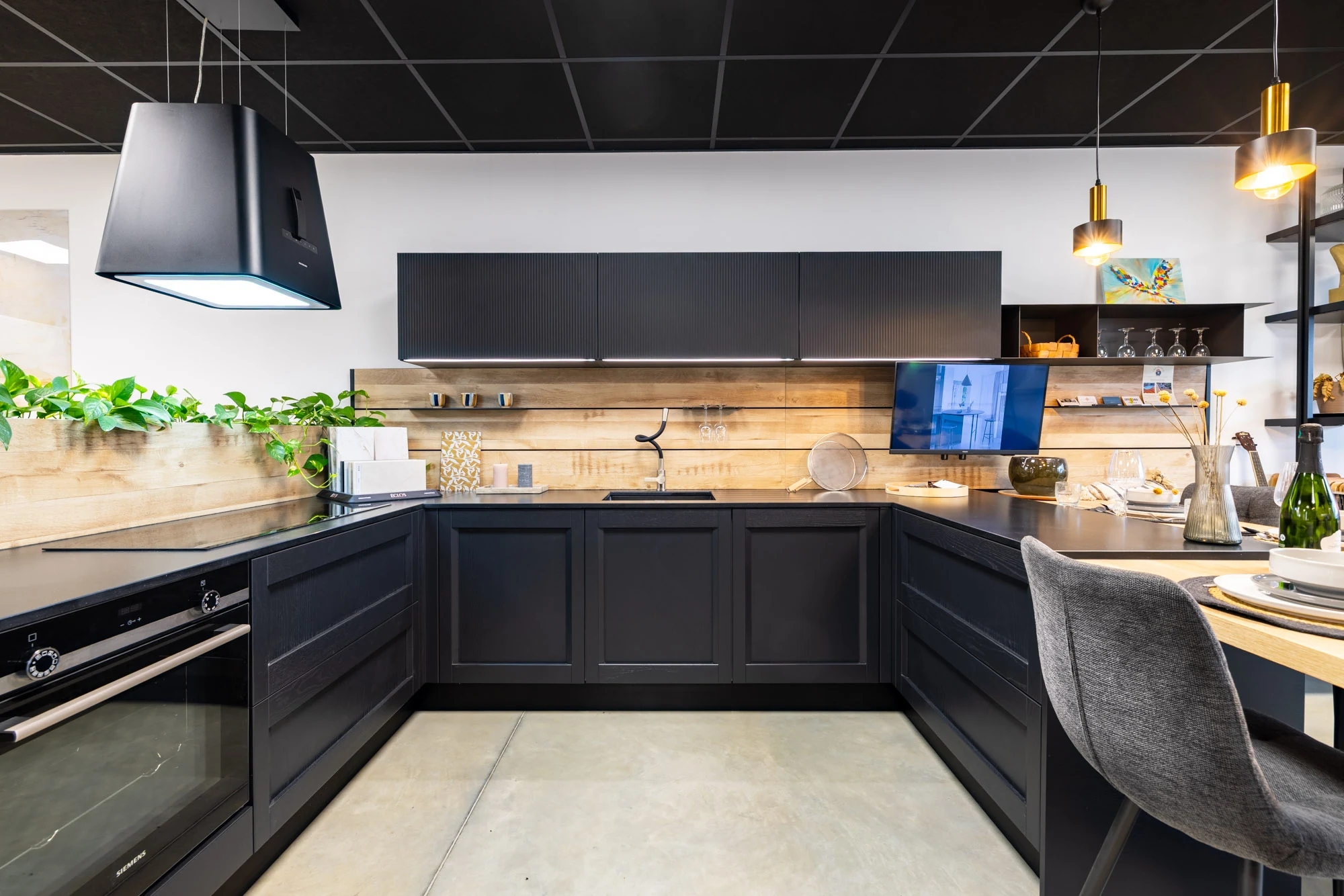 Cuisine en U aux façades noires encadrées, crédence en bois et hotte îlot noire, exposée au showroom de Portet-sur-Garonne