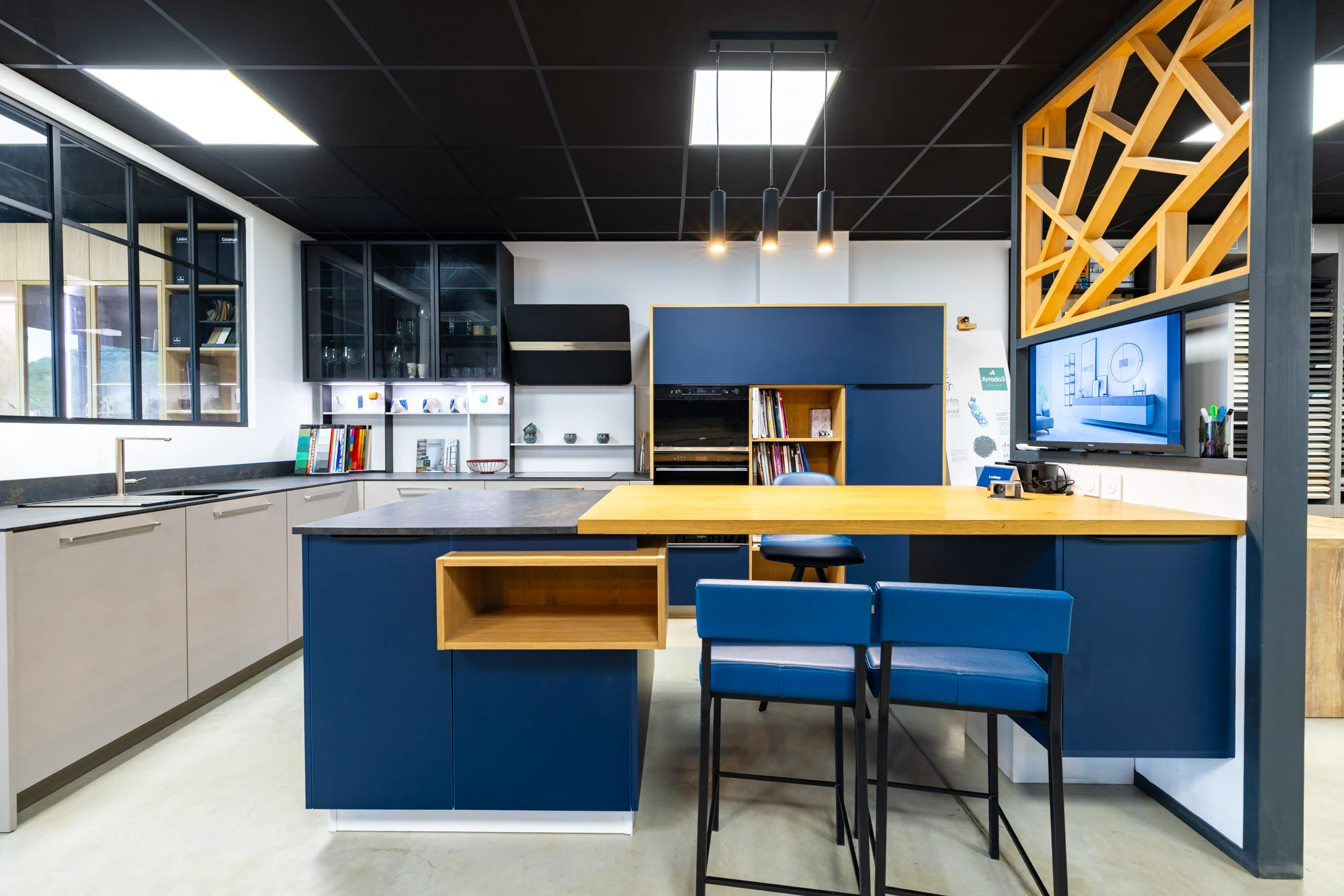 Îlot aux façades bleues prolongé par un plan en bois clair et des tabourets bleus, dans le showroom de Portet-sur-Garonne