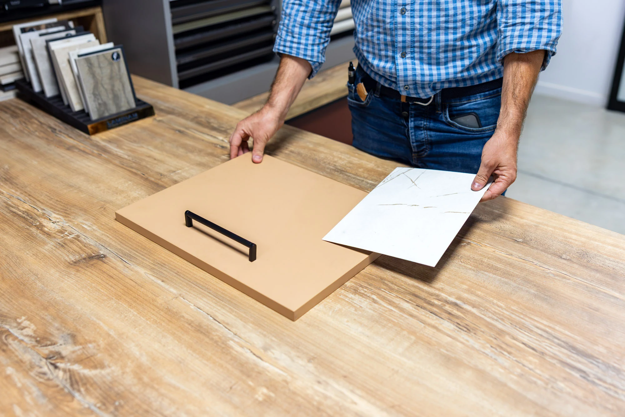 Mains d'un conseiller présentant une façade de cuisine et un échantillon de plan de travail sur une table en bois du showroom