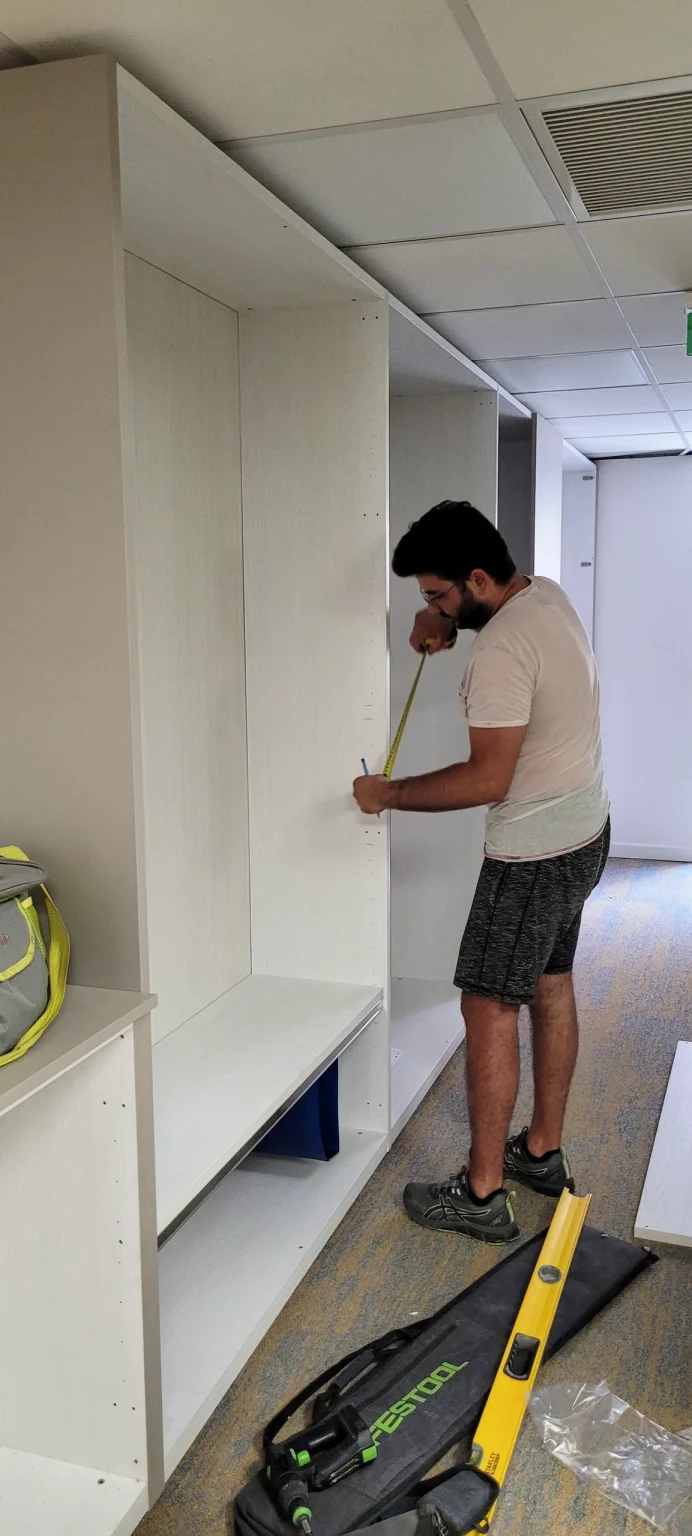 Pose d’un meuble de rangement sur mesure dans le couloir d’un bureau, ajustement en cours