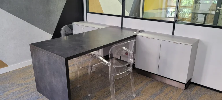 Bureau professionnel sur mesure avec plateau effet béton, chaises transparentes et cloison vitrée, réalisé par MT Cuisine