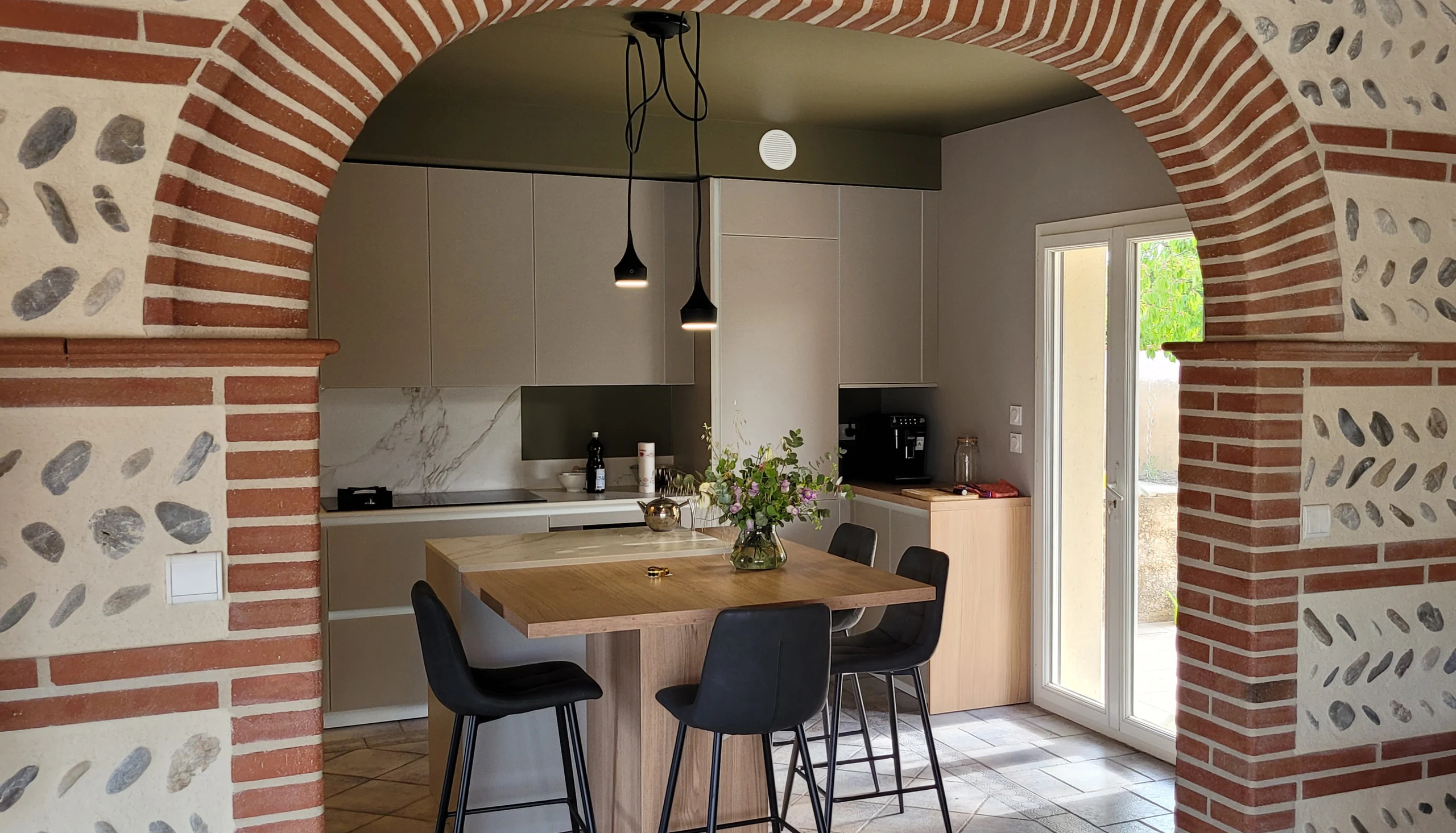 Cuisine ouverte sous une arche en brique toulousaine, avec porte-fenêtre donnant sur le jardin, réalisation MT Cuisine à Plaisance-du-Touch