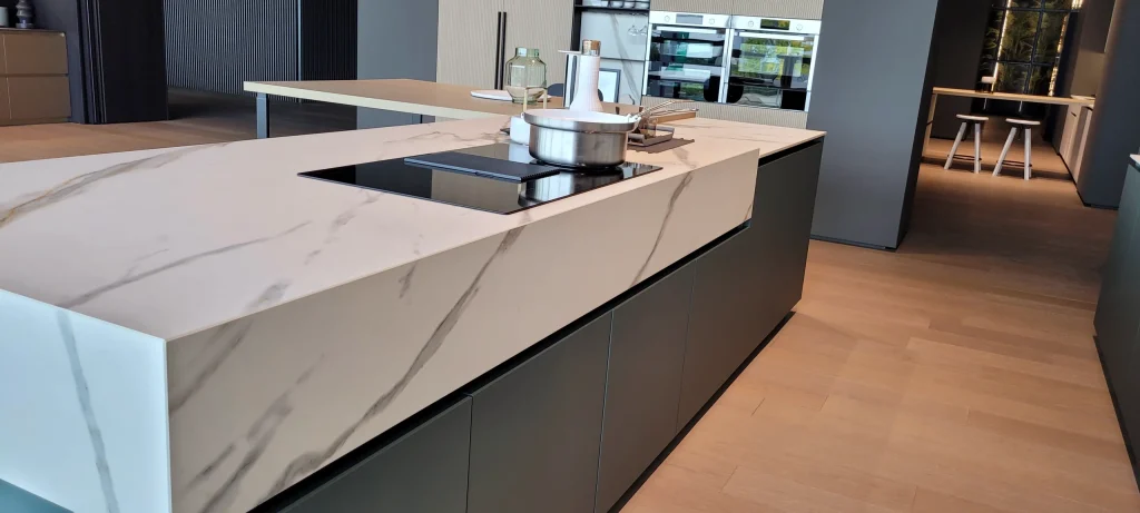 Îlot de cuisine à plan céramique effet marbre, chant à coupe d’onglet et retombée pleine hauteur, dans le showroom du fabricant