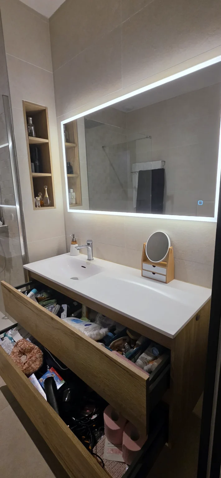 Meuble de salle de bain effet chêne aux tiroirs ouverts sous un miroir rétroéclairé