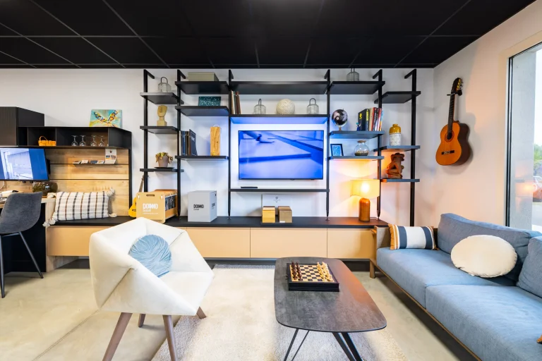 Coin salon avec canapé bleu, fauteuil blanc, table basse et étagères murales noires, showroom MT Cuisine à Portet-sur-Garonne