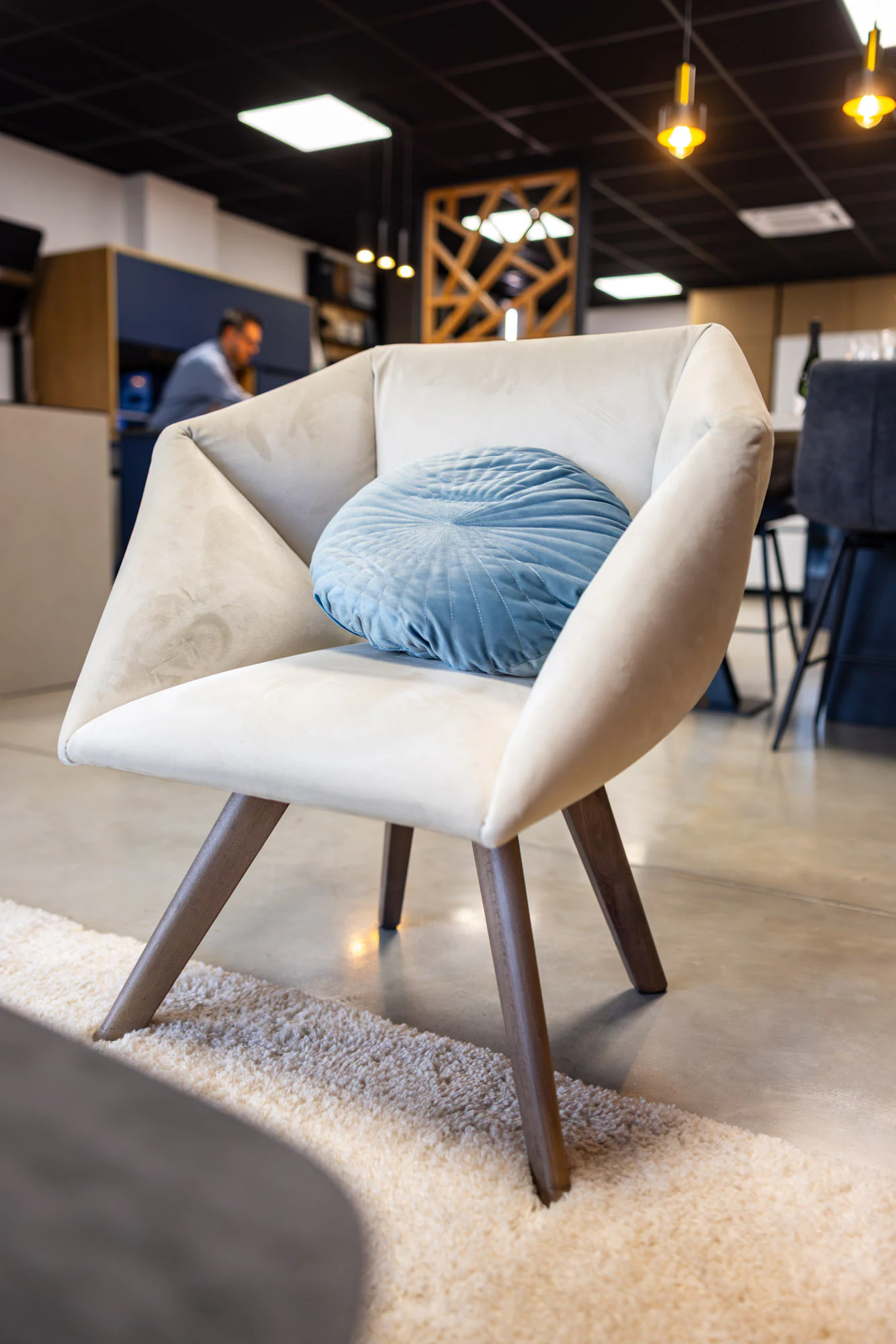 Fauteuil blanc à coussin bleu posé sur un tapis clair dans le coin d'accueil, showroom MT Cuisine à Portet-sur-Garonne
