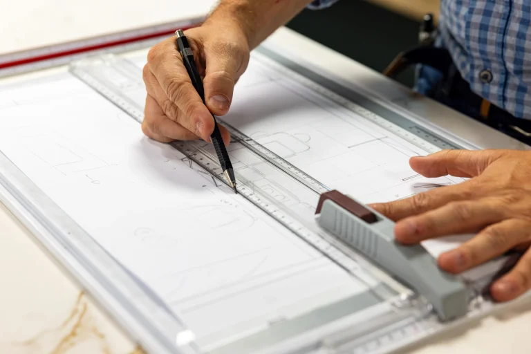 Main de Thomas traçant une esquisse au crayon et à la règle sur une planche à dessin, showroom MT Cuisine à Portet-sur-Garonne