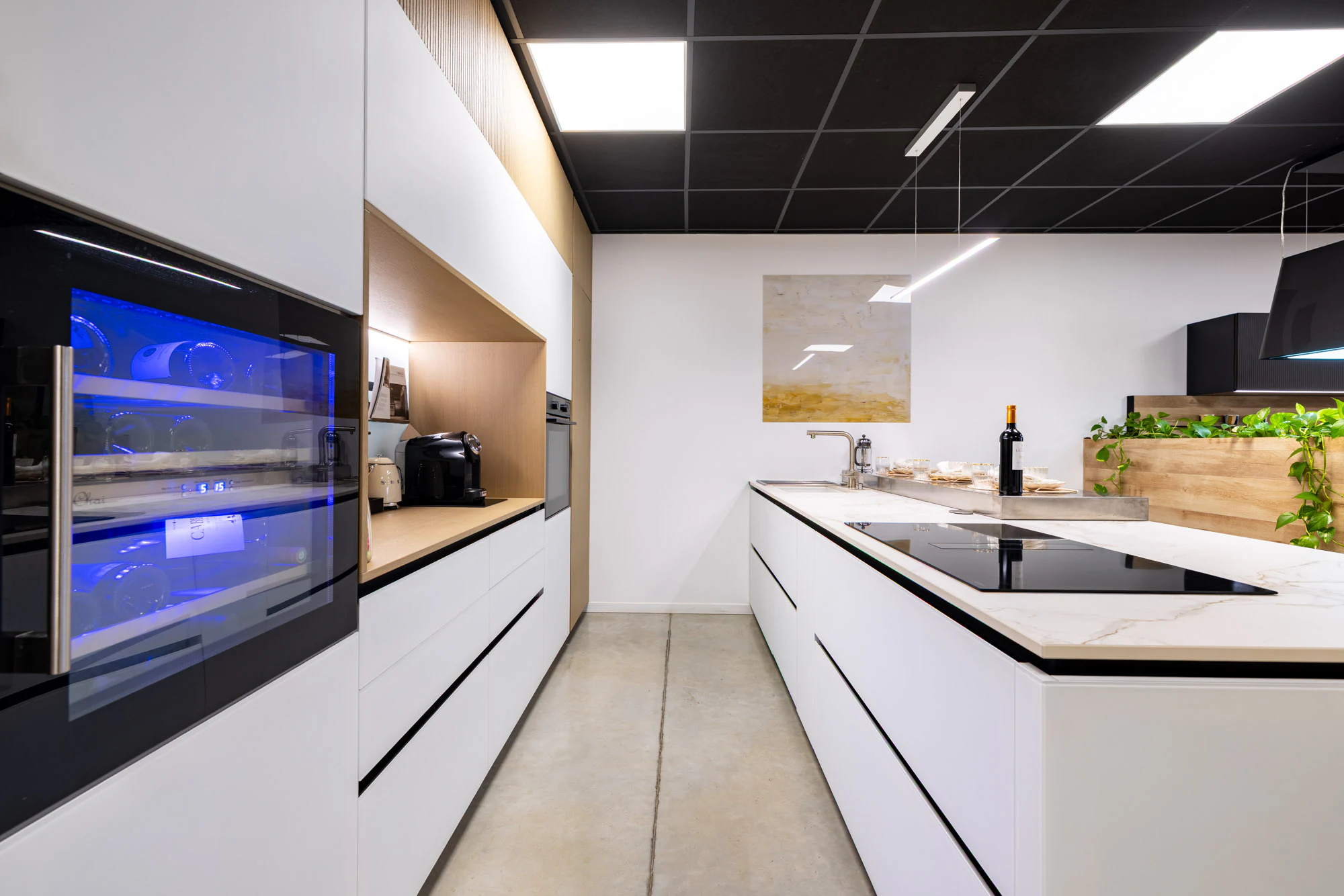 Îlot blanc à plan clair avec plaque intégrée, cave à vin encastrée et colonnes bois, showroom MT Cuisine à Portet-sur-Garonne