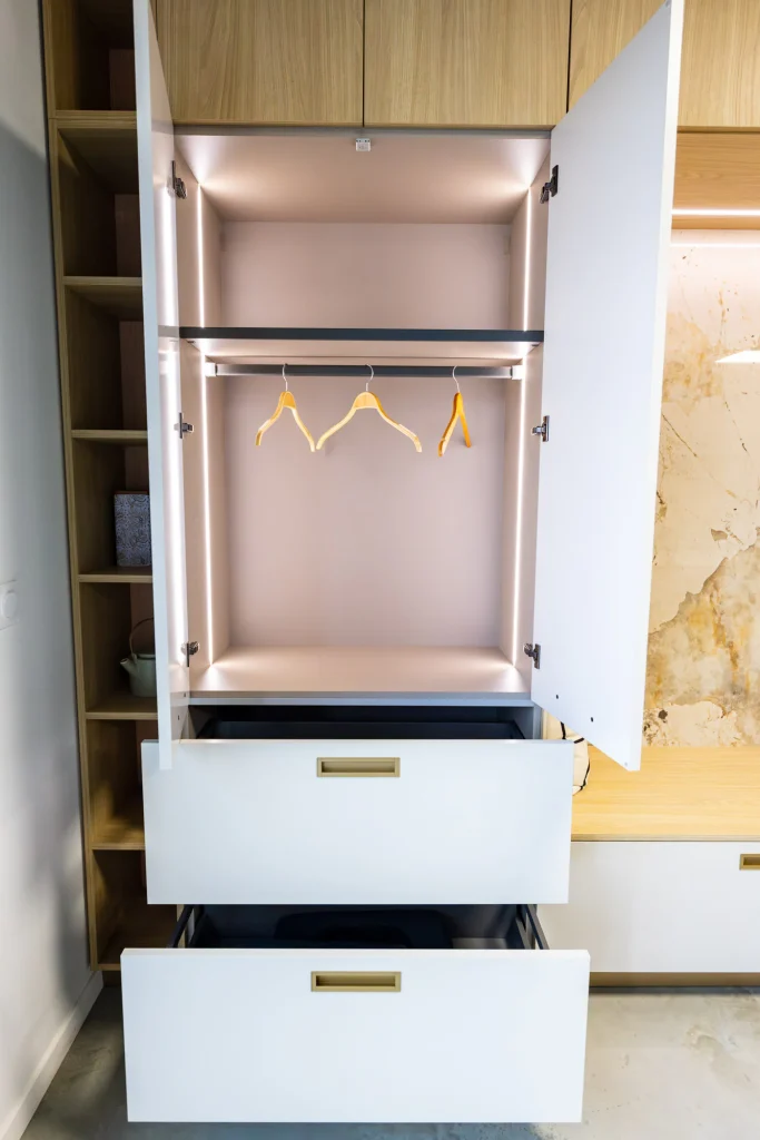 Penderie à portes ouvertes avec tringle éclairée, cintres et deux tiroirs sortis, showroom MT Cuisine à Portet-sur-Garonne