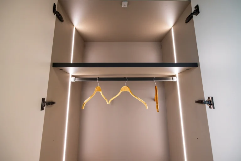Intérieur de penderie avec tringle éclairée, étagère haute et éclairage vertical sur les montants, showroom MT Cuisine à Portet-sur-Garonne