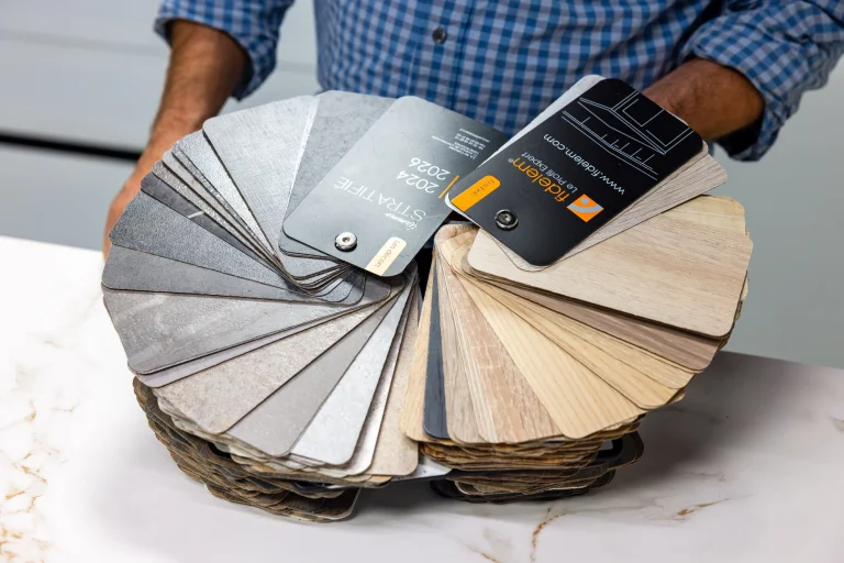 Éventail d'échantillons de finitions minérales et bois déployé en main au-dessus d'un plan clair veiné, showroom MT Cuisine à Portet-sur-Garonne