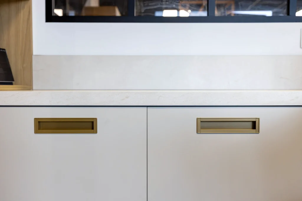 Alignement de façades claires à poignées laiton encastrées sous la jonction avec le plan de travail, showroom MT Cuisine de Portet-sur-Garonne