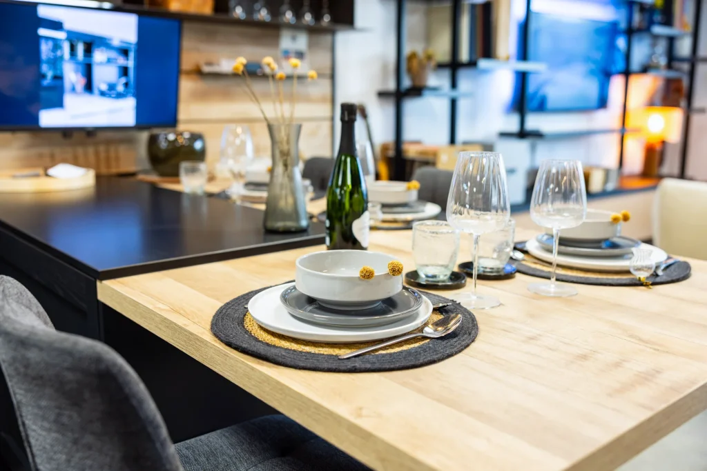 Table en bois dressée avec assiettes, verres à pied et set de table, cuisine noire en fond au showroom MT Cuisine de Portet-sur-Garonne