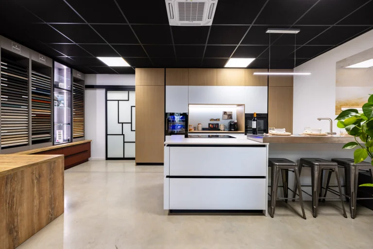 Cuisine blanche à îlot et plan bois, tabourets métal et mur d'échantillons de finitions, showroom MT Cuisine à Portet-sur-Garonne