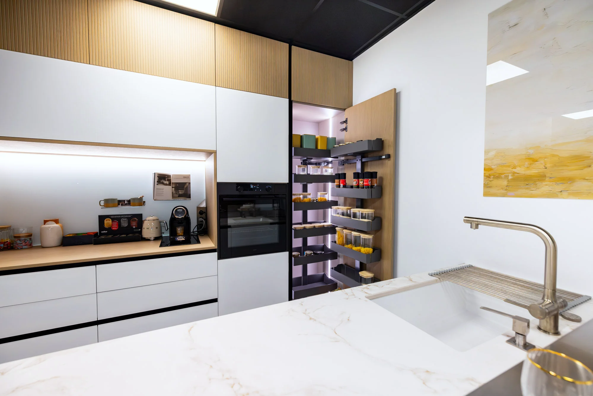 Cuisine blanche à plan veiné doré, colonne à épices éclairée et niche en bois au showroom MT Cuisine de Portet-sur-Garonne