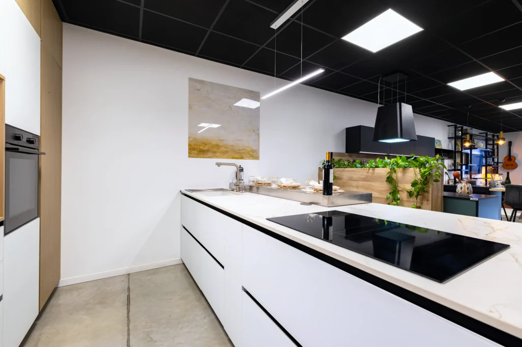 Cuisine blanche sans poignée à plan veiné clair et plaque à induction, vue d'ensemble au showroom MT Cuisine de Portet-sur-Garonne