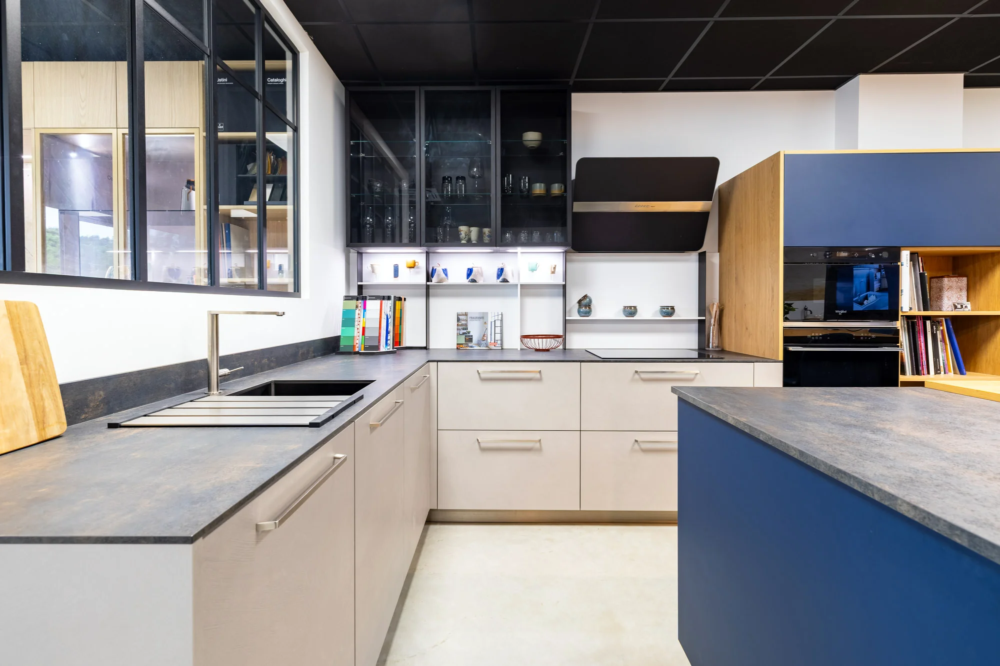 Vue d'ensemble d'une cuisine en L grise à plan foncé, vitrines noires et îlot bleu au showroom MT Cuisine de Portet-sur-Garonne