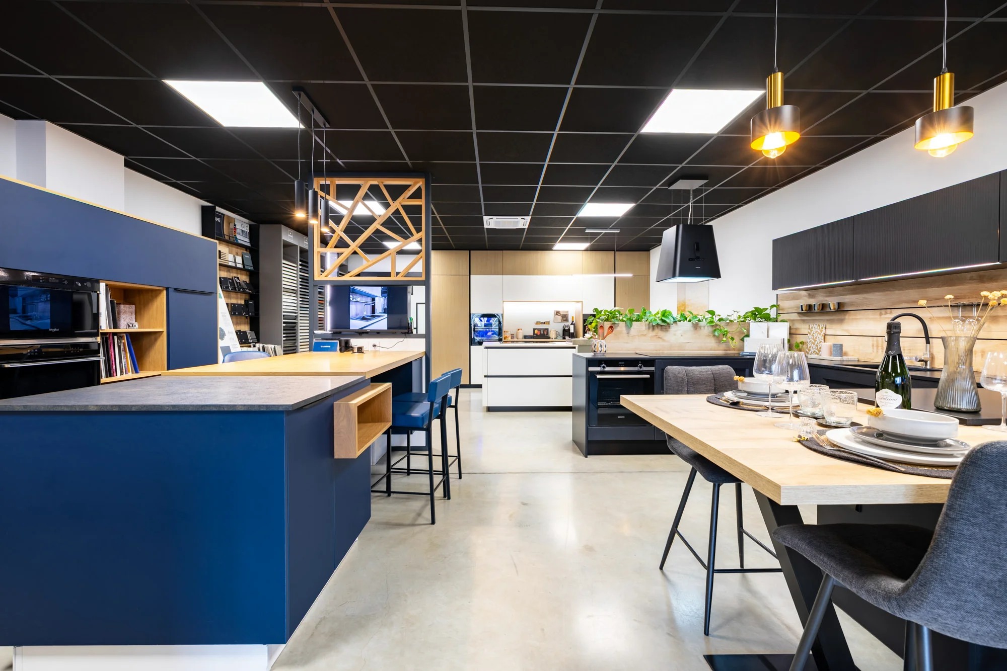 Îlot bleu à niche en bois, tabourets bleus et table haute dressée, vue d'ensemble au showroom MT Cuisine de Portet-sur-Garonne